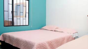 A room with a bed, a window with bars, and a teal wall.