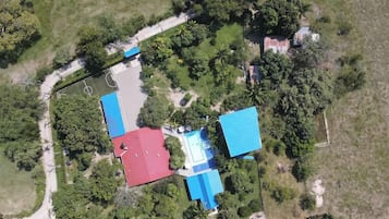 Set amidst lush greenery, this residence features a main building and a smaller structure, a paved driveway, and a tennis court.