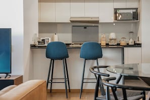 A modern kitchen with two bar stools, a glass table, and a flat-screen TV.