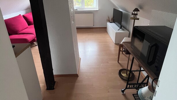 Et moderne loftværelse med skråvæg, stort vindue, fjernsyn og hyggekrog med en rød sofa.
