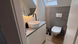 Et lille, moderne badeværelse med ovenlys, en hvid vask og et toilet.
