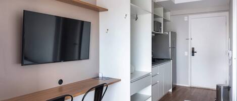 Une chambre d’hôtel moderne équipée d’un téléviseur à écran plat, d’un bureau en bois, d’une chaise, d’un lit, d’une armoire et d’une poubelle.