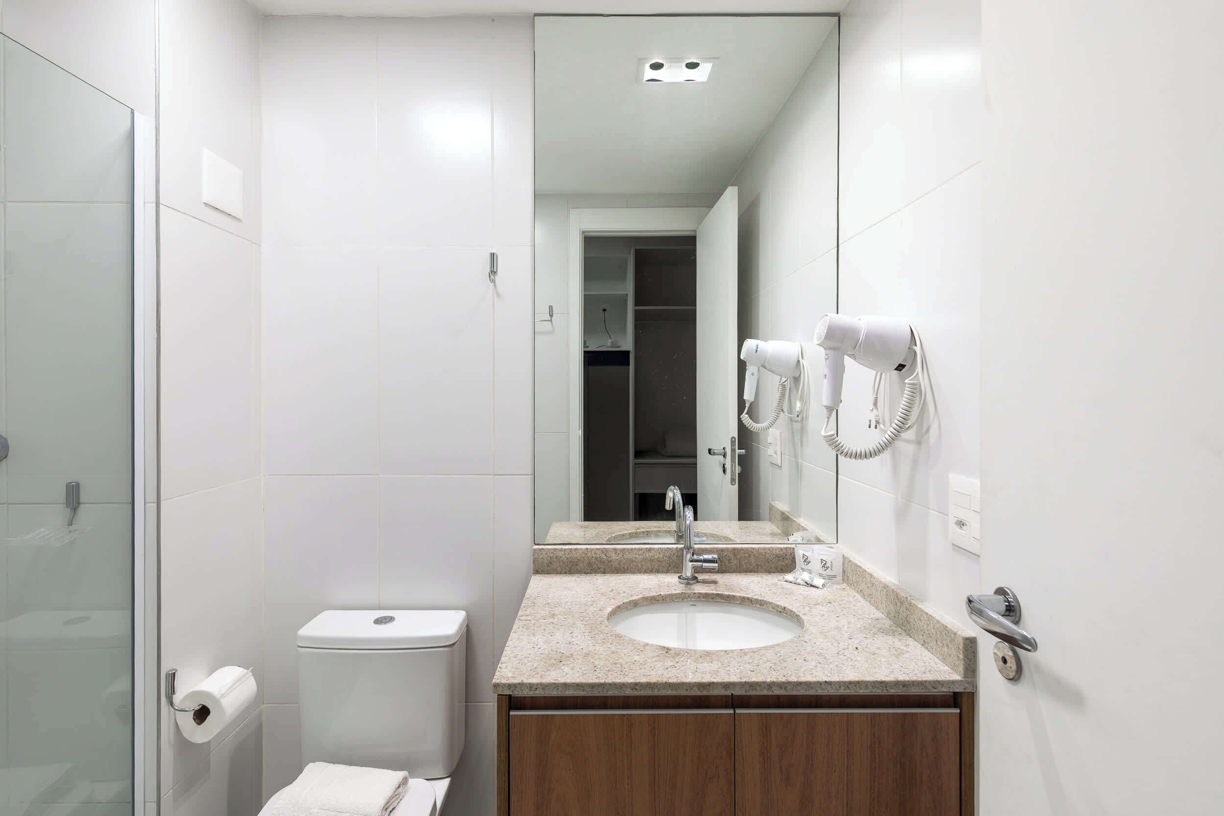 A modern bathroom with a glass shower enclosure, a toilet, a sink with a mirror, and a hairdryer mounted on the wall.