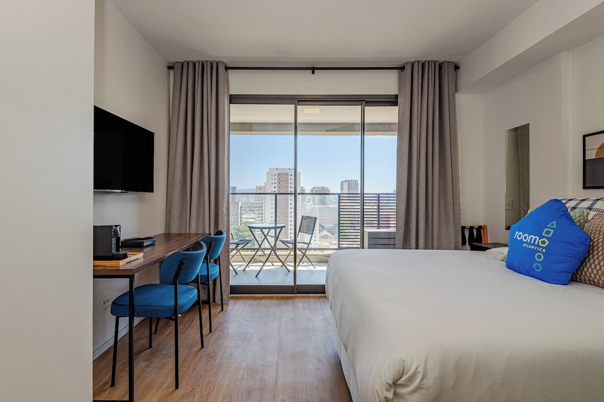 Une chambre d’hôtel comprenant un lit, un bureau avec une chaise, une télévision et un balcon avec une table et des chaises.