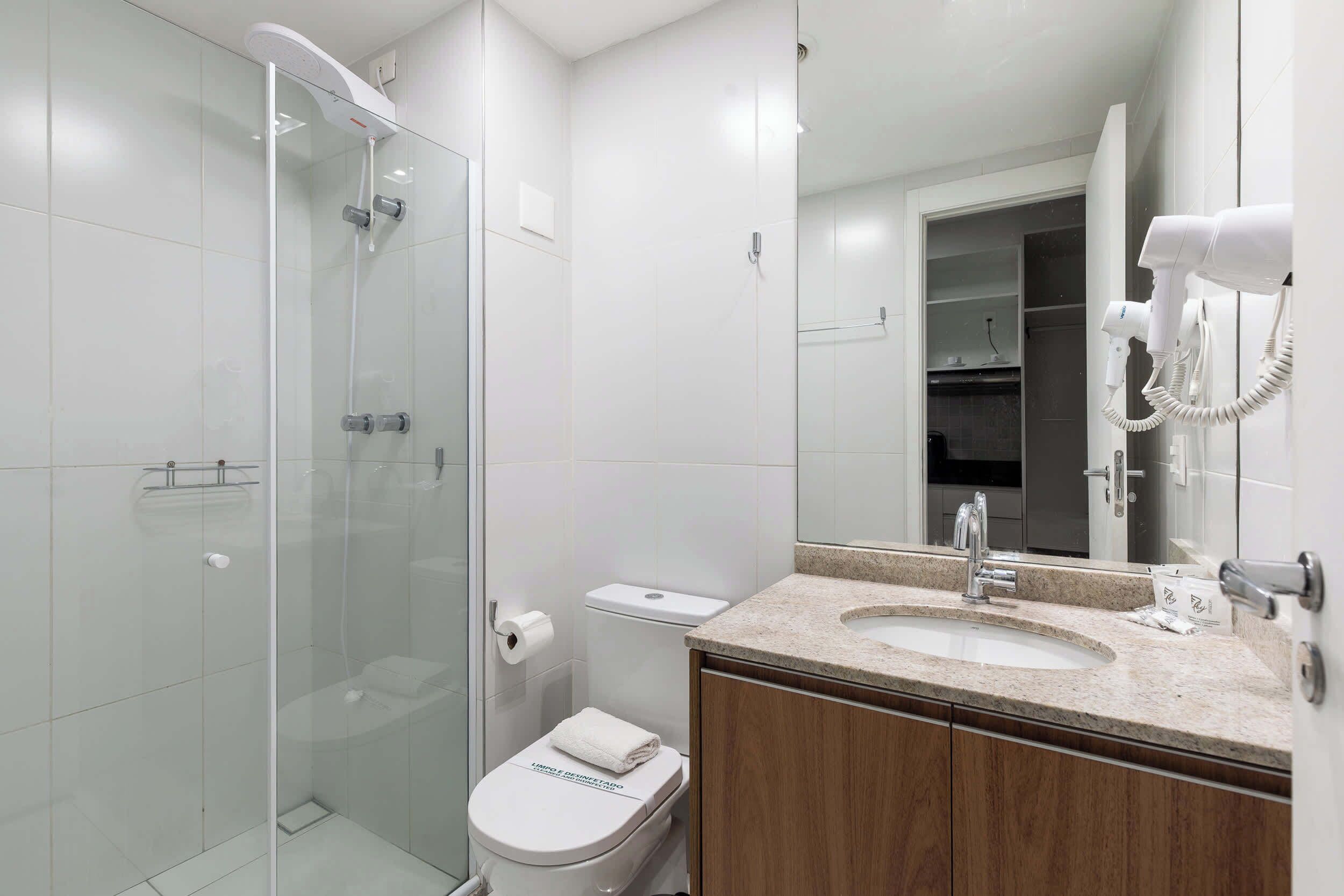 A modern bathroom with a glass-enclosed shower, a toilet with a paper towel holder, and a sink with a mirror above it.
