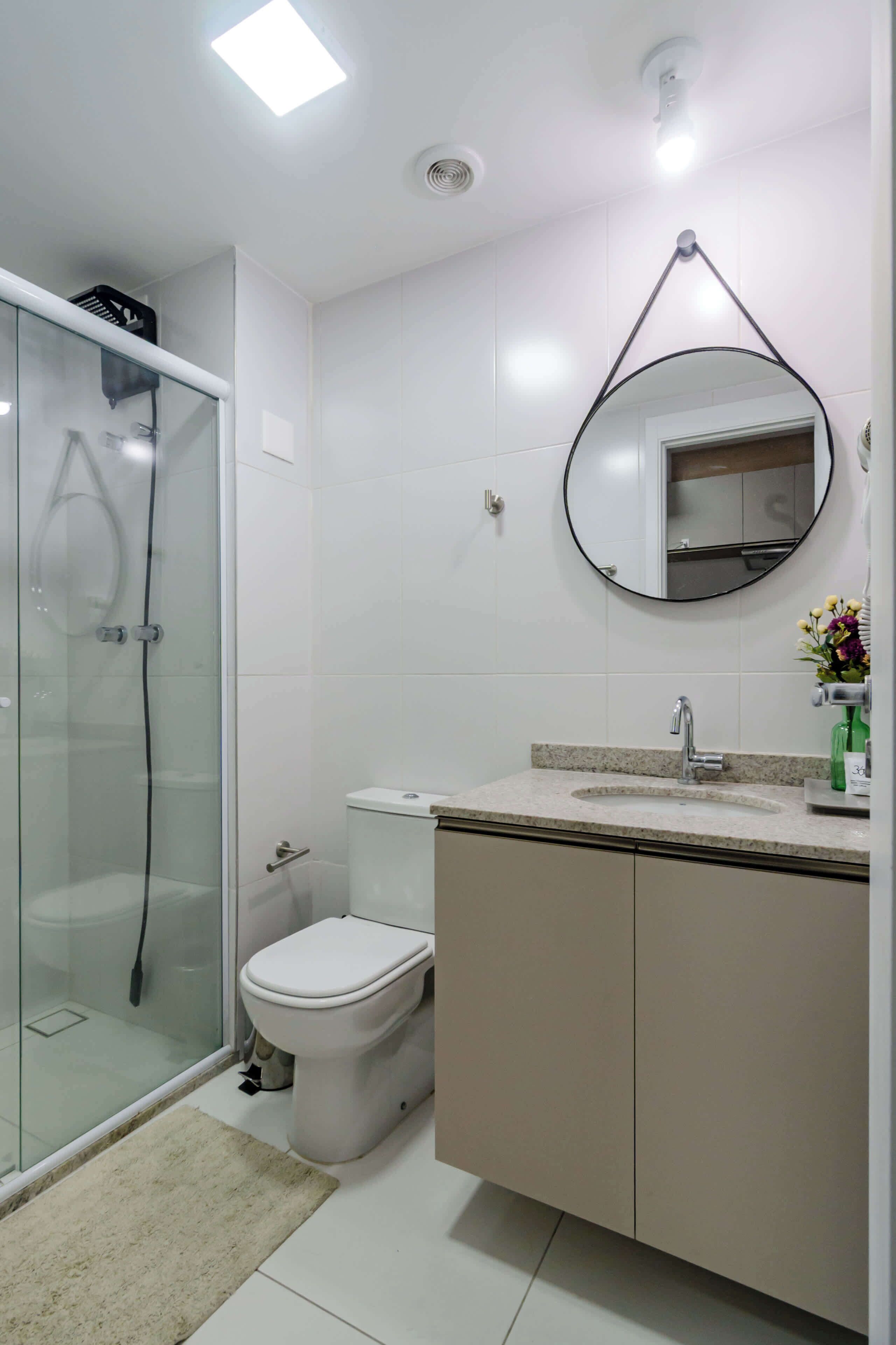 A modern bathroom with a glass shower enclosure, a toilet, a sink with a mirror, and a small vase with flowers.