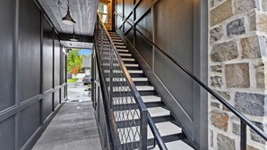Un escalier avec des rampes en métal et des murs en pierre, menant à un espace extérieur agrémenté de verdure.