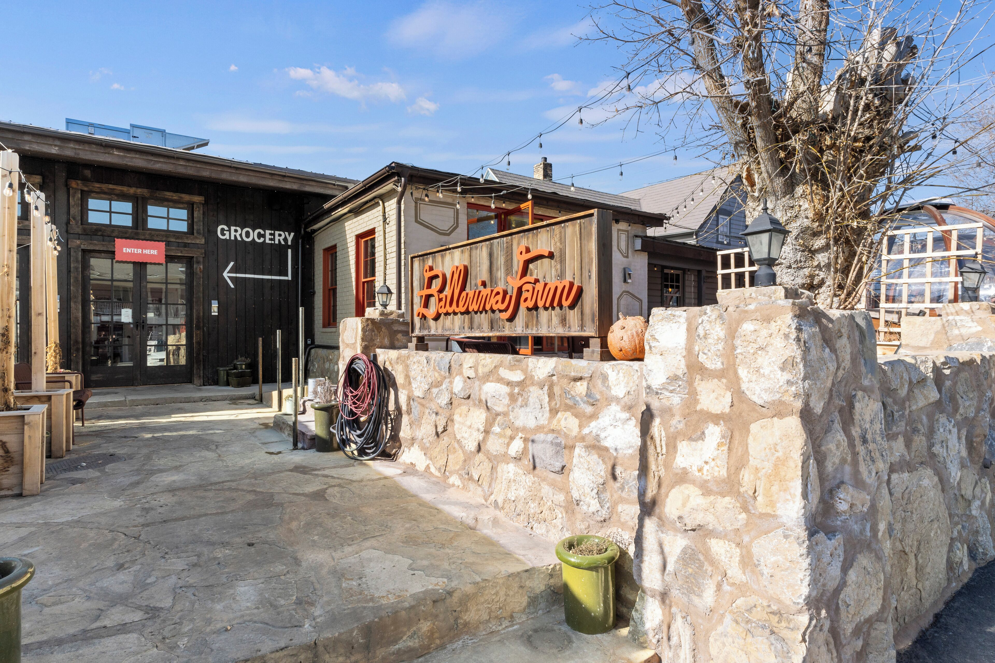 A rustic building with a 'Grocery' sign, a 'Ballina Farm' sign, and a stone wall.
