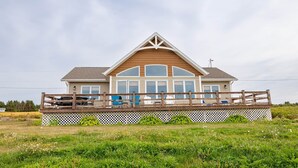 A two-story house with a large deck and a white fence. - 3-Bedroom Cavendish Oceanfront Cottage - Located inside National Park (North Rustico)