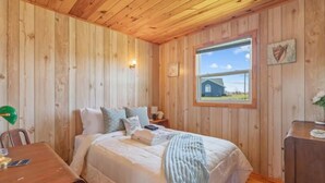A wooden-paneled room with a bed, a table, and a window with a view of a barn.