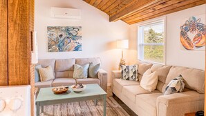 Ein gemütliches Wohnzimmer mit Holzbalkendecke, einem beigefarbenen Sofa, einem blauen Couchtisch und zwei abstrakten Bildern.