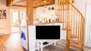 Eine moderne Küche mit weißen Schränken, einer Holztreppe und einem Flachbildfernseher auf einem weißen Lowboard.