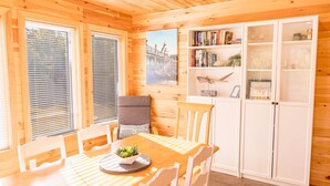 Ein Zimmer mit Holzwänden, einem Esstisch, Stühlen, einem Bücherregal und einem Schrank.