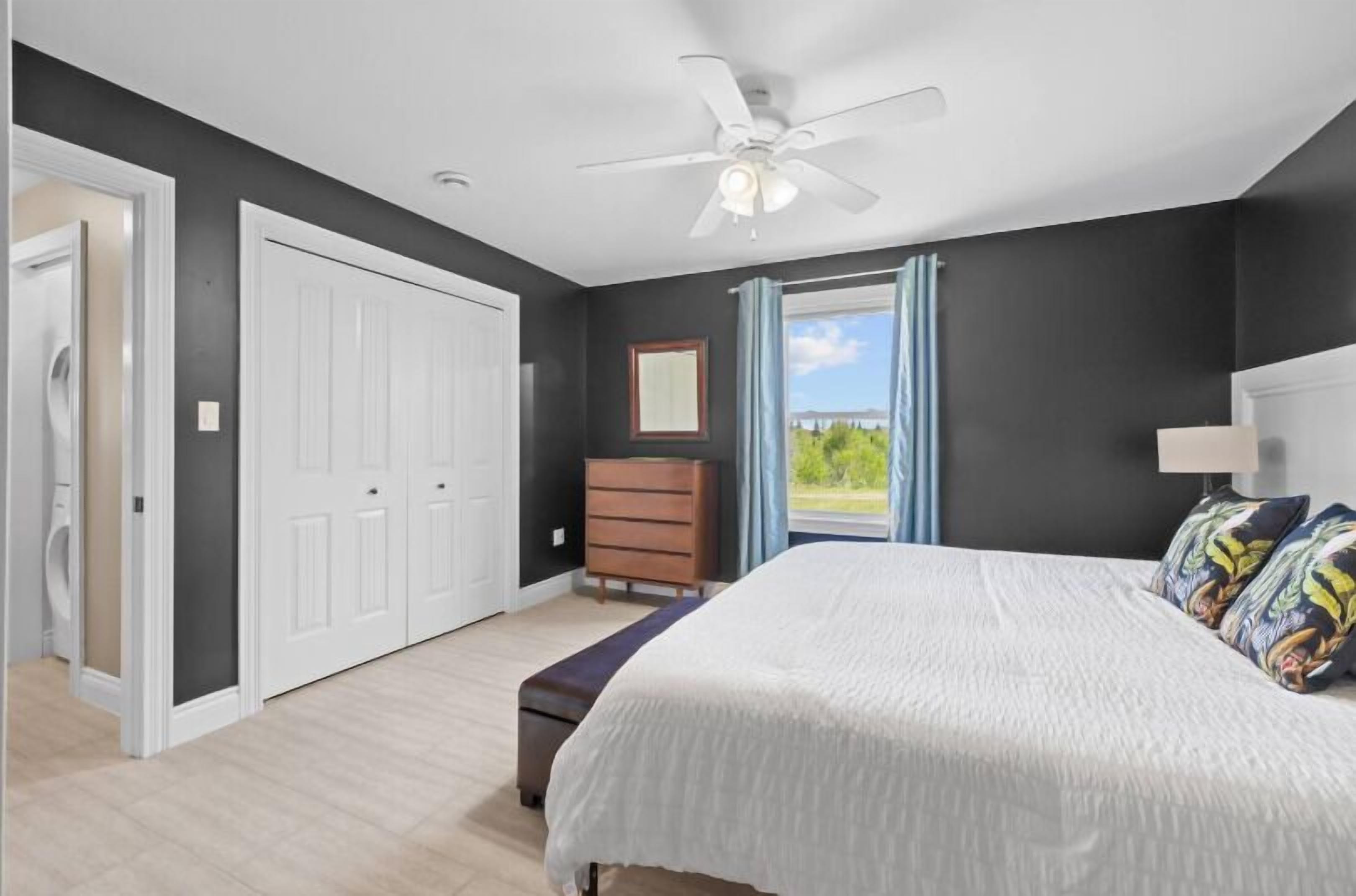 A bedroom with a bed, a dresser, a ceiling fan, and a window with curtains.