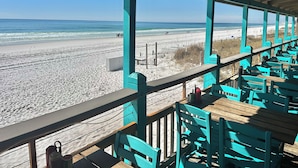 Un restaurant situé en bord de mer, avec une terrasse, une vue sur la plage et une plateforme en bois.