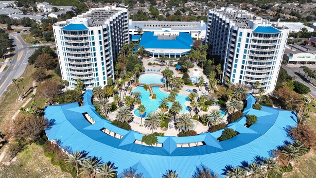 Un complexe hôtelier doté d’une piscine centrale, entouré de palmiers et d’un bâtiment au toit bleu.