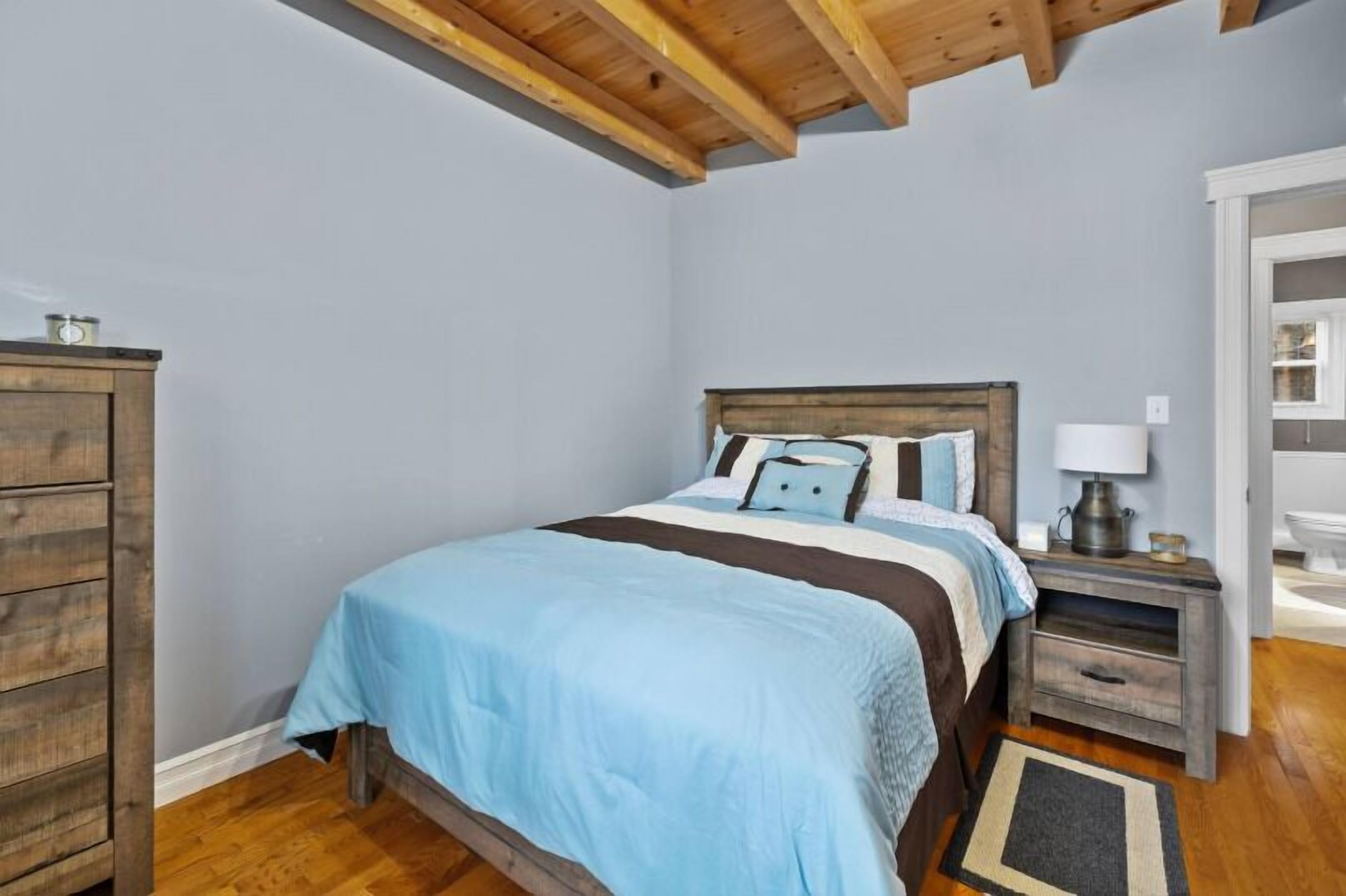 A bedroom with a bed, wooden headboard, nightstand, dresser, and a door leading to another room.