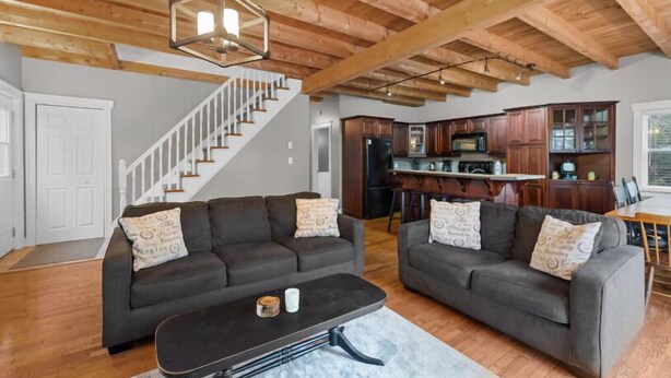 A spacious living room with two dark sofas, a coffee table, and a staircase leading to another level. - 3-Bedroom Chalet with Kayak in private community - minutes to Cavendish Beach (North Rustico)