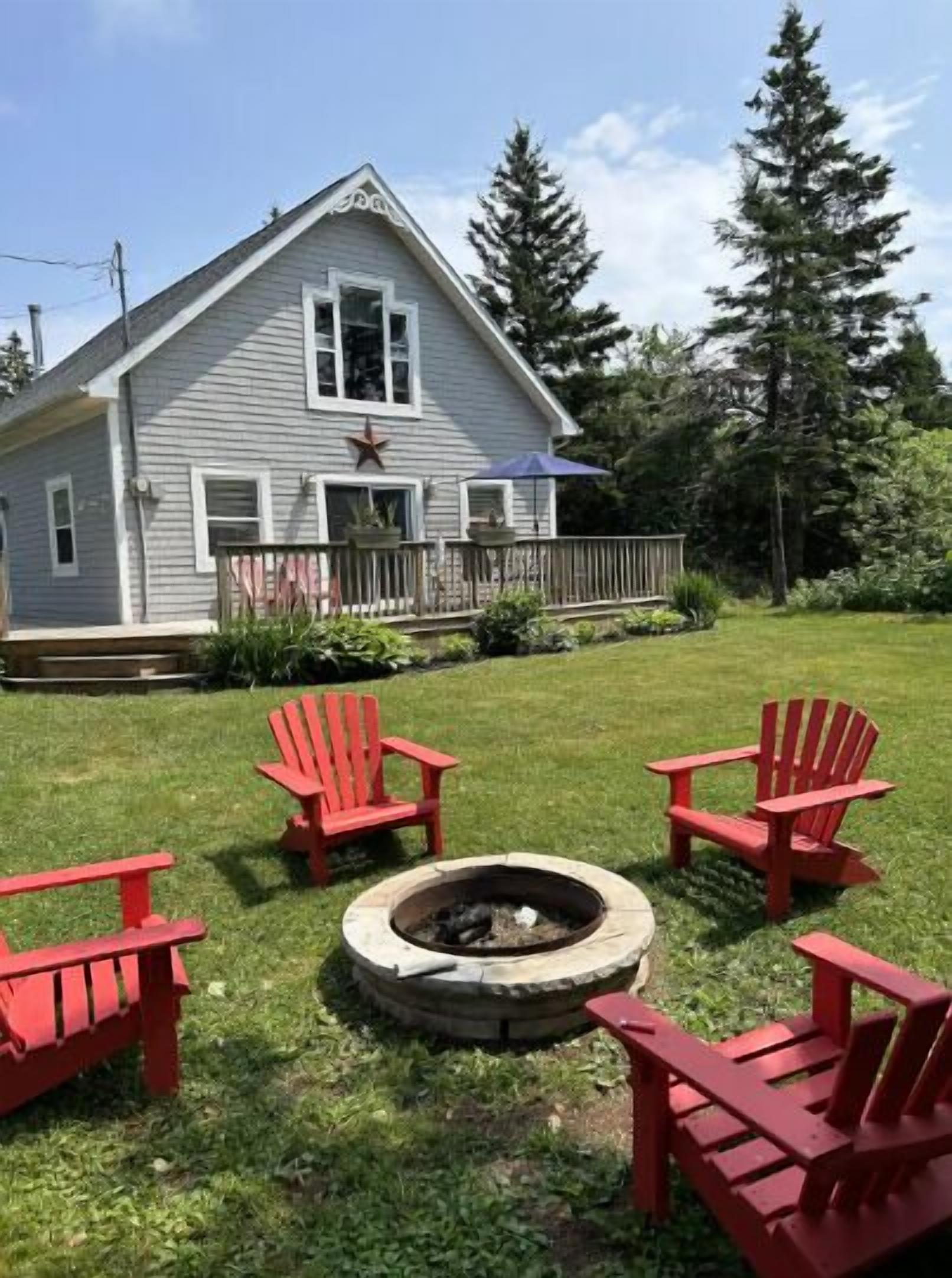 Una casa con porche, una fogata y sillas Adirondack rojas.