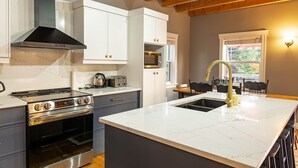 A modern kitchen with white cabinets, a stainless steel range, and a large island with a sink. - 3-Bedroom Chalet with Kayak in private community - minutes to Cavendish Beach (North Rustico)