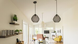 Een moderne woonruimte met een eethoek, keuken en zithoek. Er zijn hangende pendantlampen, een flatscreen-tv en een plant op een plank.