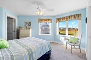 Une chambre à coucher comprenant un lit, une chaise, une commode et une fenêtre donnant sur une maison et des champs.
