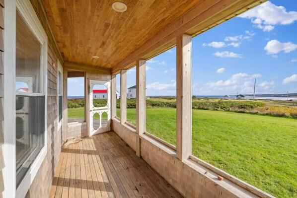 A wooden covered porch with large windows overlooking a grassy landscape.
