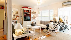 A cozy living room with a white sofa, a white coffee table, a striped rocking chair, and a bookshelf filled with books and decorative items. - Bayside Breeze with Beach Access (Prince Edward Island)
