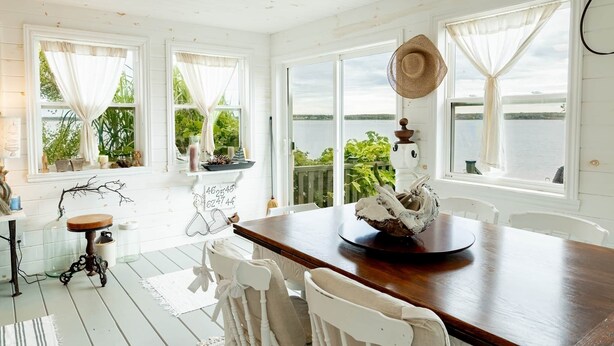 A dining area with a wooden table, white chairs, and a view of a lake. - Bayside Breeze with Beach Access (Prince Edward Island)