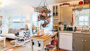 A kitchen with a hanging pot rack, a dining area with a white sofa, and a view of the water outside. - Bayside Breeze with Beach Access (Prince Edward Island)