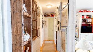 A narrow hallway with wooden shelves, a white door at the end, and a small red house model on top. - Bayside Breeze with Beach Access (Prince Edward Island)