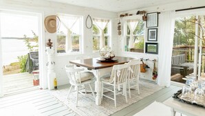 A coastal room with a wooden dining table, white chairs, and a view of the sea. - Bayside Breeze with Beach Access (Prince Edward Island)