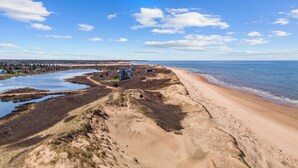 A coastal landscape with a sandy beach, a small body of water, and a few buildings. - Family-Friendly Beach House on PEI with Steps to Private Sandy Beach (Morell)