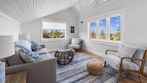 A spacious living room with a high ceiling, large windows, a ceiling fan, and a view of the outdoors. - Family-Friendly Beach House on PEI with Steps to Private Sandy Beach (Morell)