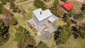 An aerial view of a two-story house with a large deck, a circular patio, and a separate garage. - Family-Friendly Beach House on PEI with Steps to Private Sandy Beach (Morell)