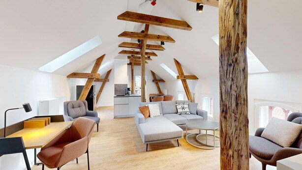 Un loft espacioso con techos altos, vigas de madera a la vista y una cocina moderna al fondo.