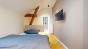 Un dormitorio con cama, estructura de vigas de madera, televisor y una puerta que da a otra habitación.