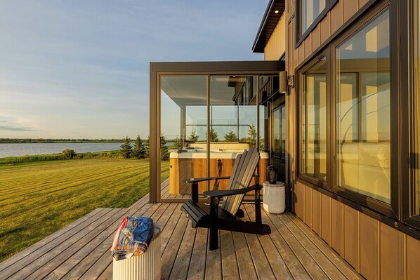 A modern outdoor deck with a hot tub, a chair, and a blanket.