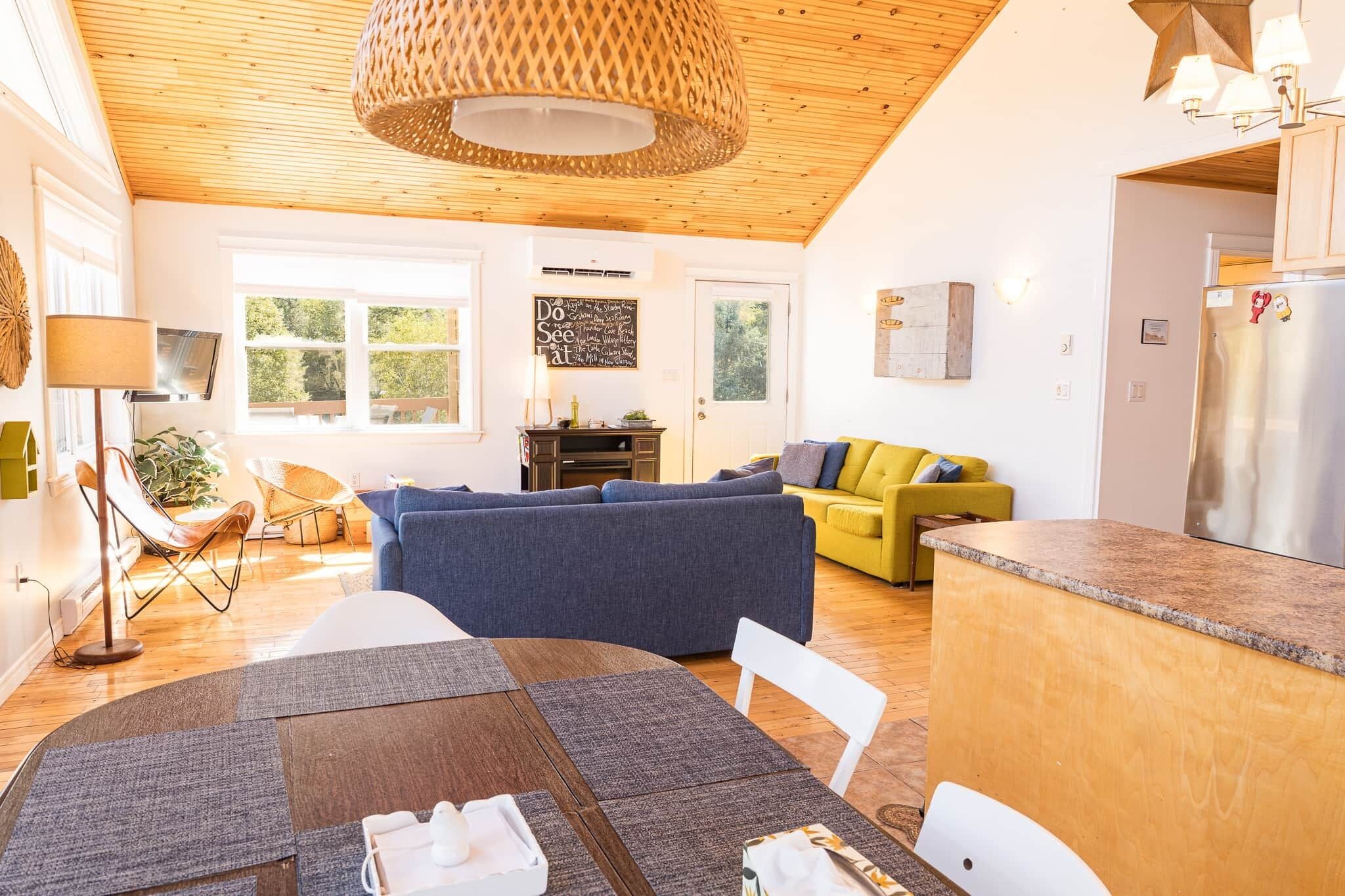 Eine moderne Küche mit Holzbalkendecke, einem Essbereich mit Tisch und Stühlen, einer Couch und einem gelben Sessel.