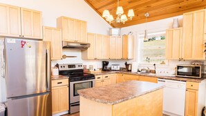 A modern kitchen with wooden cabinets, stainless steel appliances, and a granite countertop island. - Riverside Summer Retreat on PEI with Hot Tub, Deck, Kayaks & Pet-Friendly Stay (Prince Edward Island)