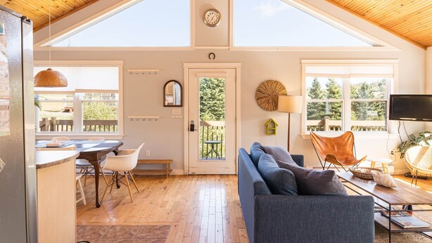 A spacious living area with a high ceiling, large windows, a dining area, and a cozy seating arrangement. - Riverside Summer Retreat on PEI with Hot Tub, Deck, Kayaks & Pet-Friendly Stay (Prince Edward Island)