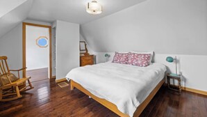 Un dormitorio con cama de madera, paredes blancas y techo inclinado.