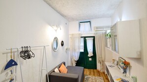 A small, well-lit room with a bed, a desk with a chair, a mirror, and a wardrobe.