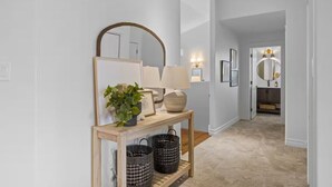 A hallway with a wooden console table, a mirror, wall sconces, and a door leading to another room. - Stylish Stratford Home Near Charlottetown—Spacious, Family-Friendly Retreat (Stratford)