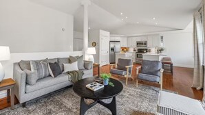 A modern living room with a grey sofa, a black coffee table, and a kitchen in the background. - Stylish Stratford Home Near Charlottetown—Spacious, Family-Friendly Retreat (Stratford)