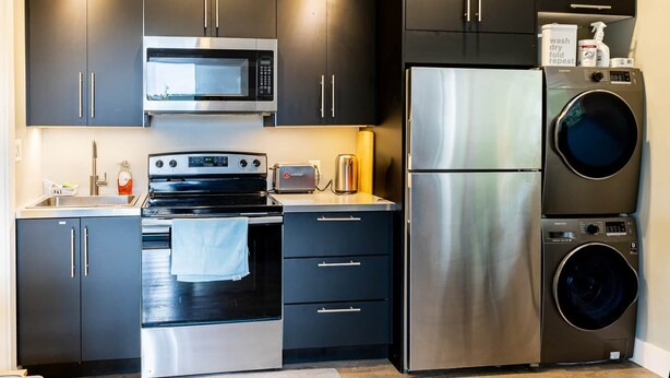 Una cocina moderna con electrodomésticos de acero inoxidable, incluyendo un microondas, horno y refrigerador, además de lavadora y secadora integradas.