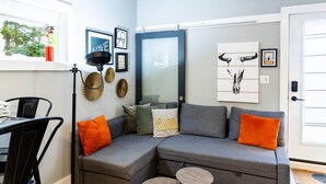 Una sala moderna con un sofá seccional gris, una mesa de comedor con sillas y un amplio ventanal con persianas.