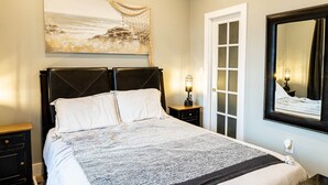Un dormitorio con cama, mesita de noche, lámpara, puerta y un espejo grande.