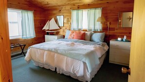 A wooden cabin bedroom with a bed, nightstands, a lamp, and a sailboat model.