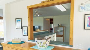 A wooden counter with a decorative bowl and a tissue box. A mirror reflects a kitchen area with a wooden shelf and a framed picture.